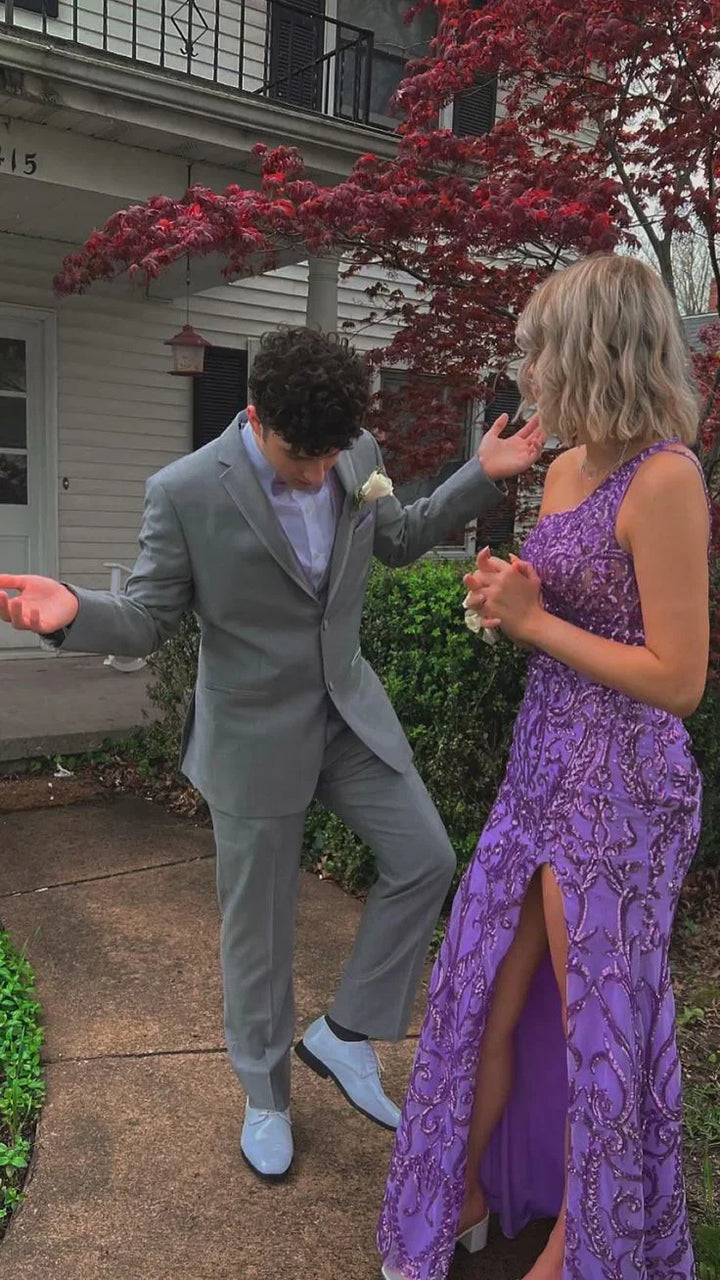 Young couple in formal attire, man in gray suit and woman in purple beaded dress, standing outside house near red-leafed tree