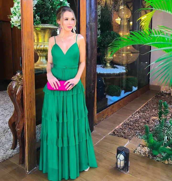 Woman in a green tiered dress with pink clutch standing by glass door, ZAPDRESS fashion