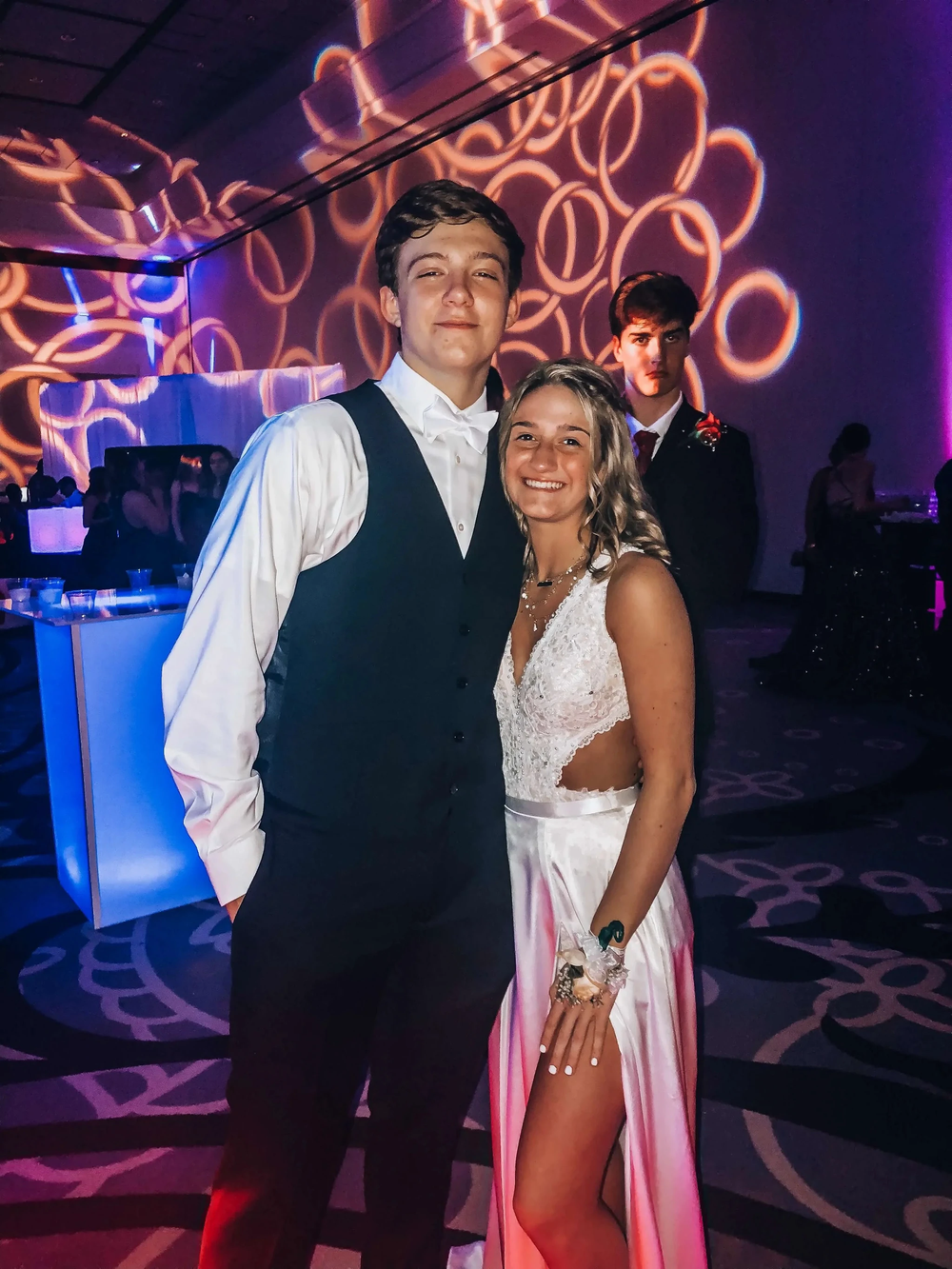 Young couple in formal attire at a dance event with patterned lighting, ZAPDRESS themed