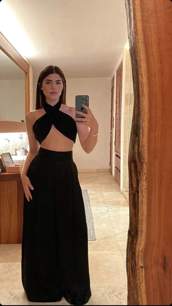 Woman taking mirror selfie wearing black crisscross crop top and high-waisted pants in modern room