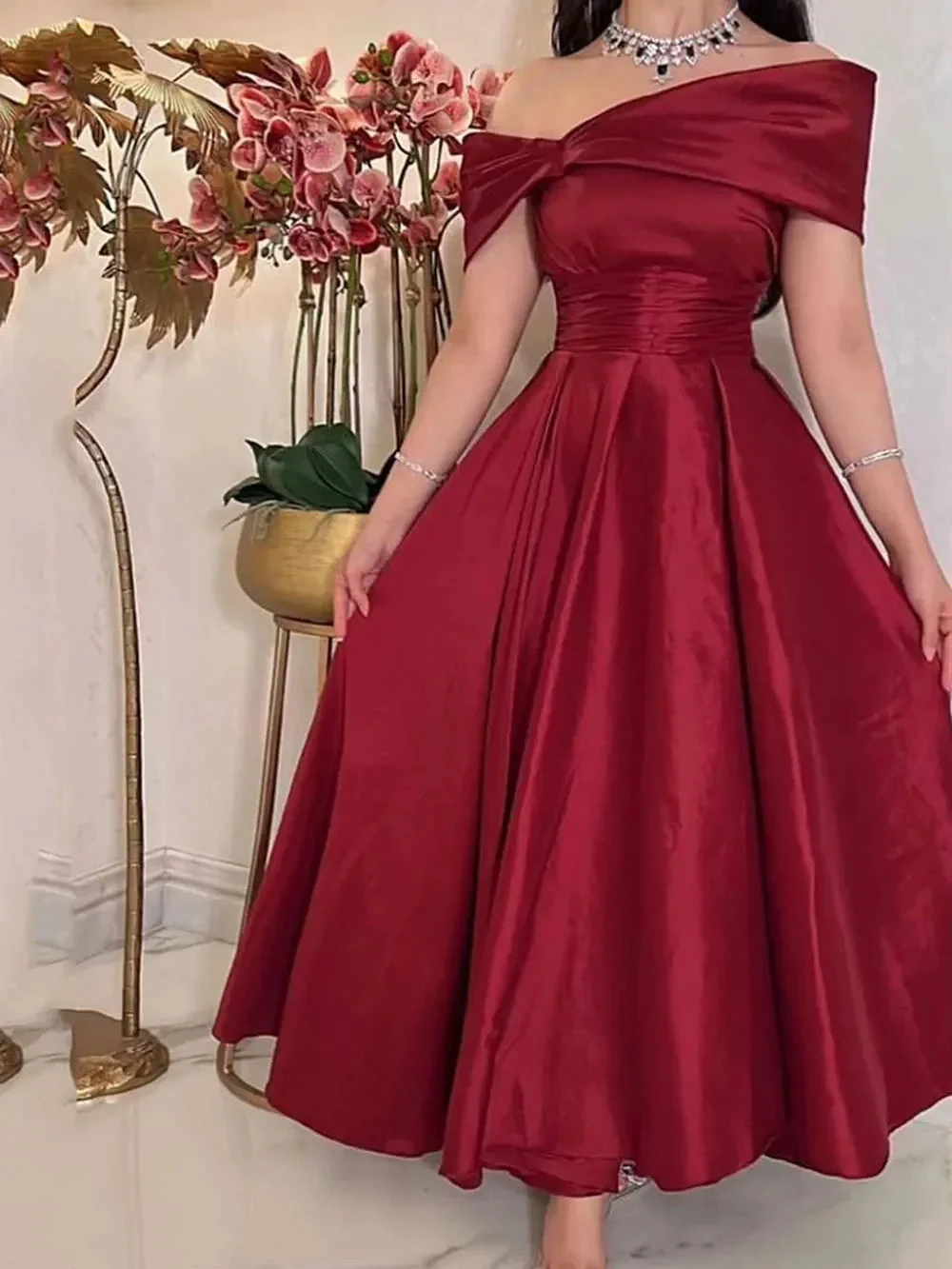 Elegant woman in off-shoulder red satin dress with floral backdrop at ZAPDRESS