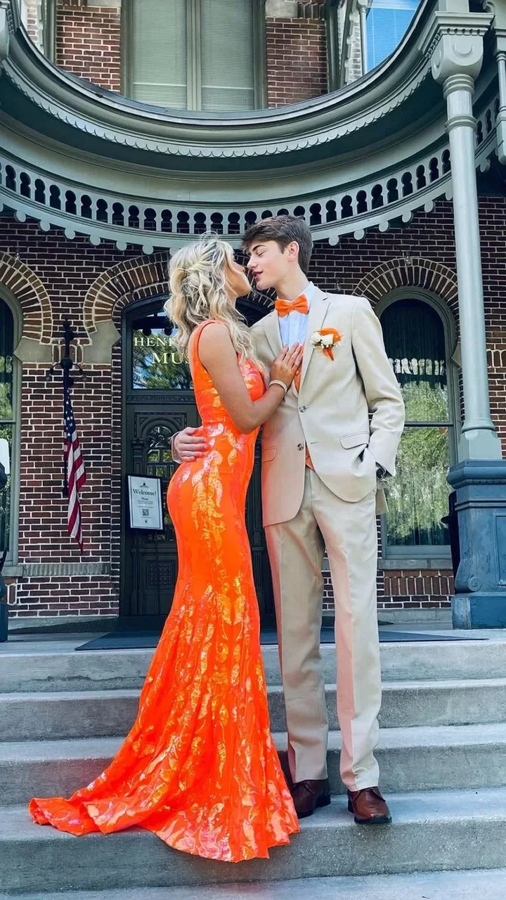 Couple posing on steps, woman in a bright orange formal dress, man in beige suit, ZAPDRESS fashion