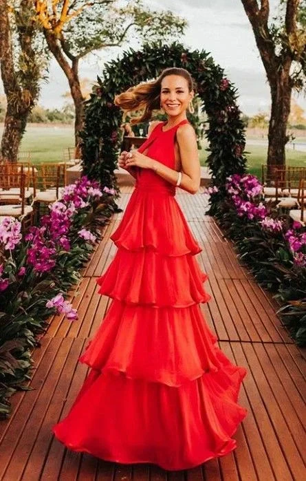 Woman in elegant red tiered dress from ZAPDRESS, standing on flower-lined outdoor walkway