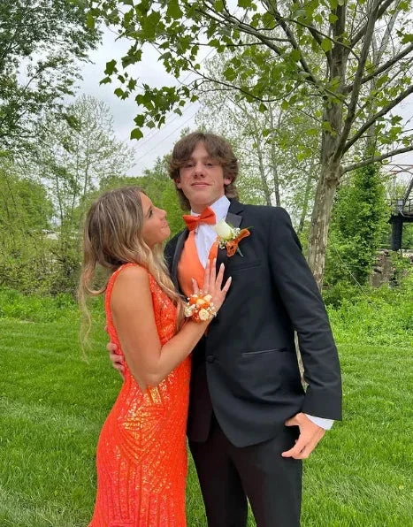 Young couple in formal attire, orange dress and tuxedo, posing outdoors for ZAPDRESS