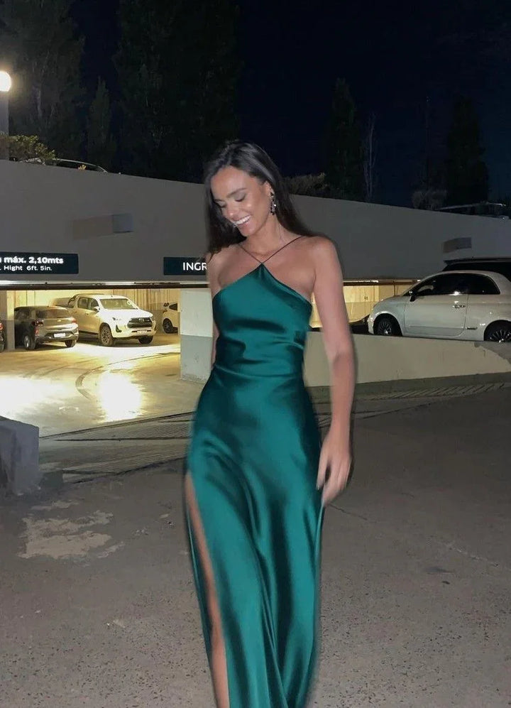 Woman in a green satin evening dress with thigh-high slit, smiling outdoors at night