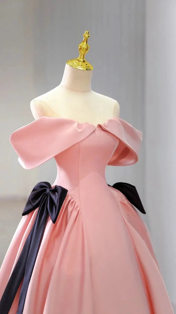 Elegant pink off-shoulder ball gown with black bows on mannequin at ZAPDRESS