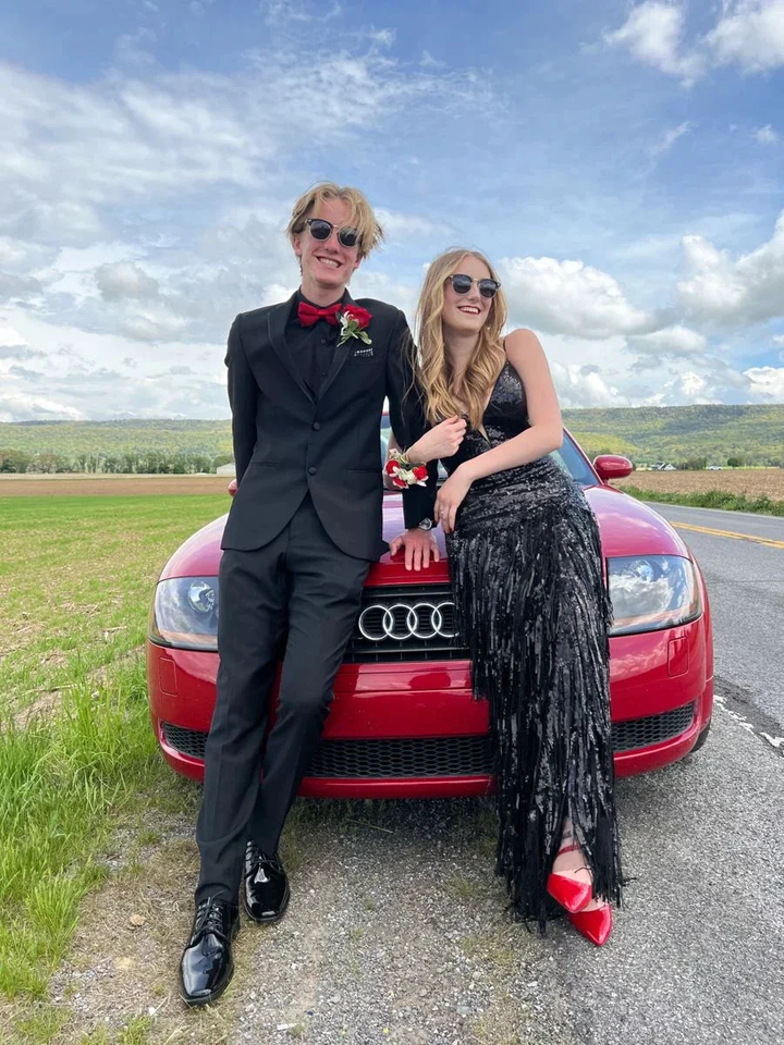 Couple in formal black outfits posing by red Audi car outdoors, ZAPDRESS style