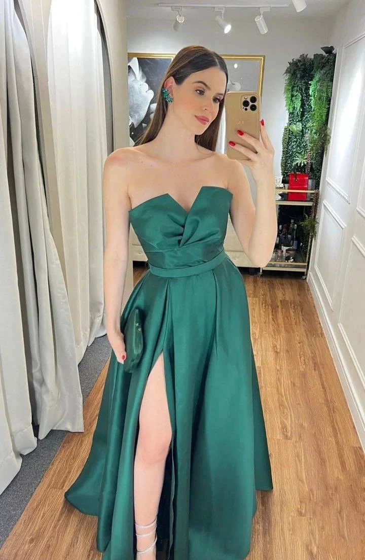 Woman in a strapless emerald green evening gown with a thigh-high slit, taking a mirror selfie in a boutique fitting room on wooden flooring, ZAPDRESS fashion.