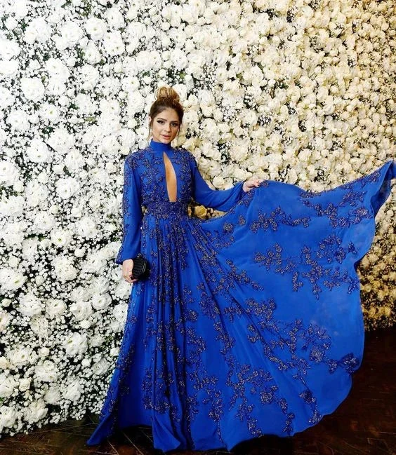 Woman in an elegant blue embellished gown posing by a wall of white flowers at ZAPDRESS