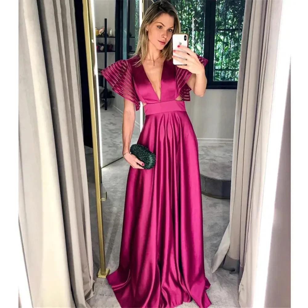 Woman taking mirror selfie wearing a fuchsia satin evening gown in a modern room
