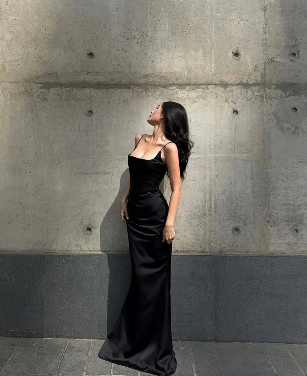 Woman in elegant black evening gown poses against concrete wall, ZAPDRESS fashion