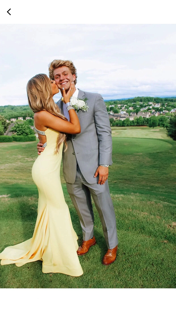 Woman in yellow formal dress kisses man in grey suit on grass, ZAPDRESS fashion style