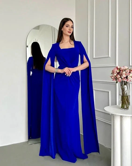 Woman in elegant royal blue cape evening gown stands in modern room, ZAPDRESS fashion
