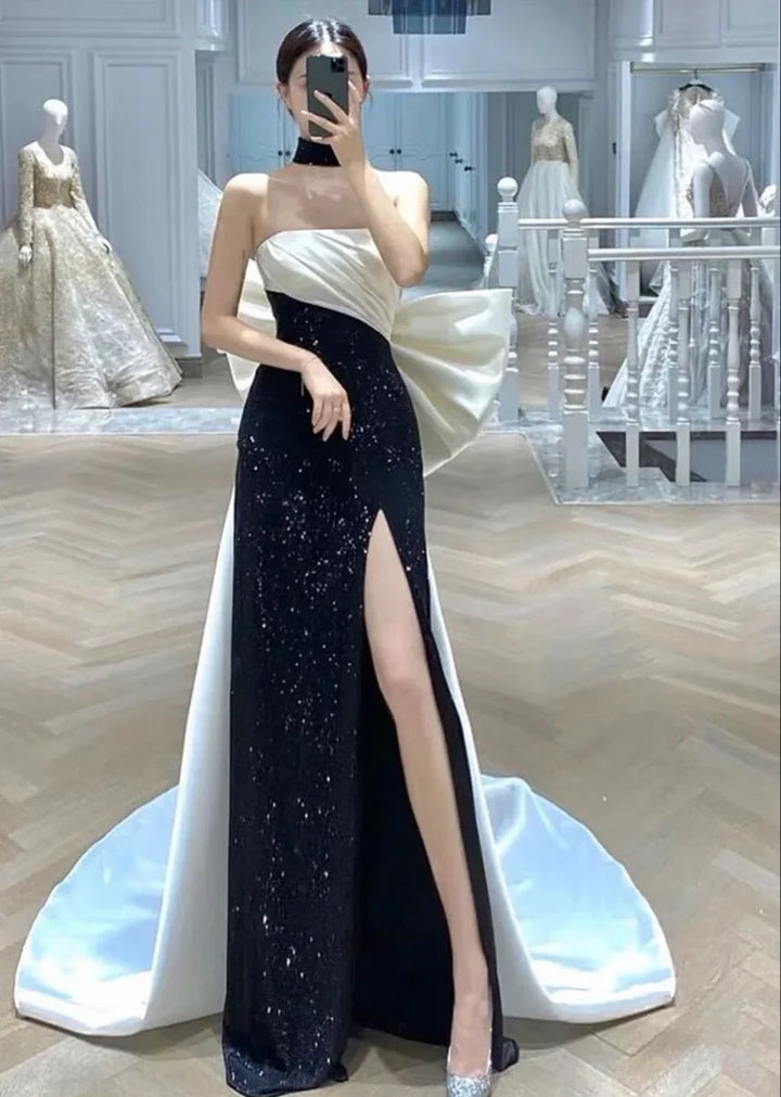 Woman modeling elegant black and white evening gown with high slit at ZAPDRESS boutique
