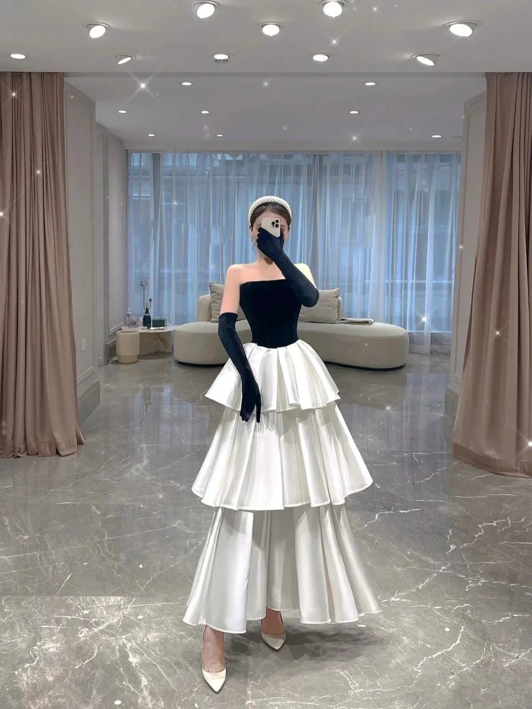 Elegant woman in a tiered black and white evening dress with gloves in a modern living room, ZAPDRESS fashion