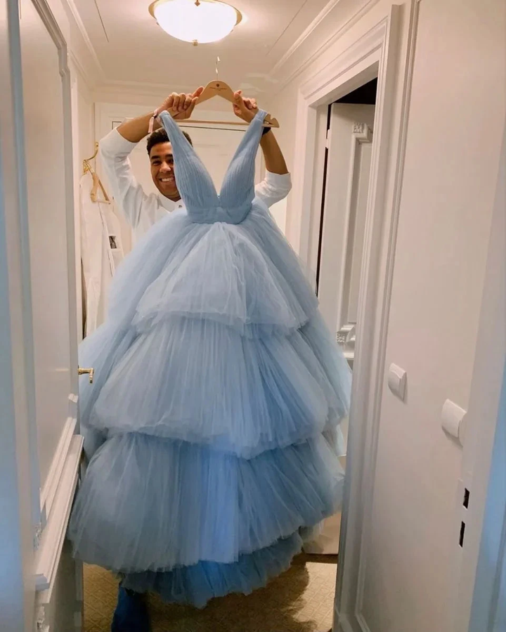 Smiling man holding a tiered blue tulle ballgown dress in a well-lit hallway, Zapdress