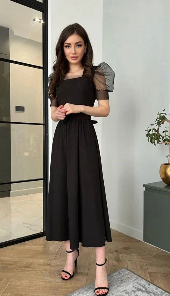 Woman in elegant black midi dress with sheer puff sleeves, standing indoors, ZAPDRESS fashion