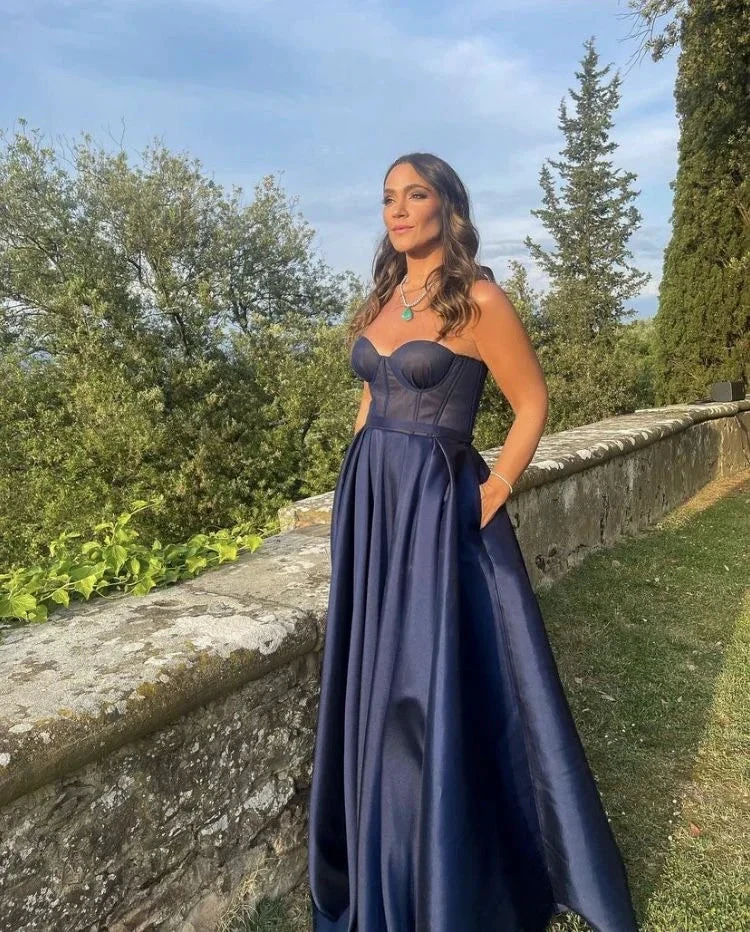 Woman in elegant navy blue gown standing outdoors by stone wall, ZAPDRESS fashion