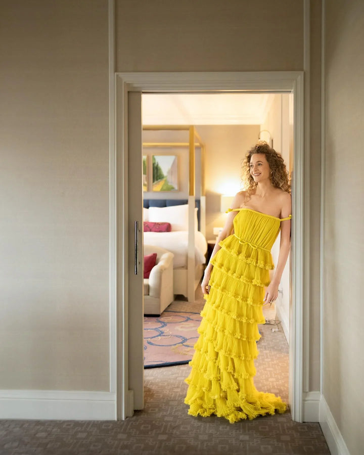 Woman in bright yellow ruffled dress standing in doorway, elegant bedroom behind, ZAPDRESS fashion