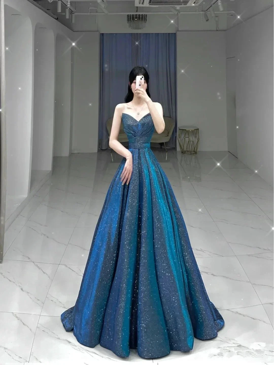Woman in shimmering blue strapless evening gown posing in modern showroom, ZAPDRESS fashion