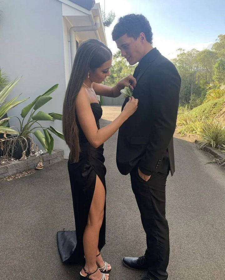 Young woman in a black prom dress pins boutonniere on man in suit outdoors, ZAPDRESS style