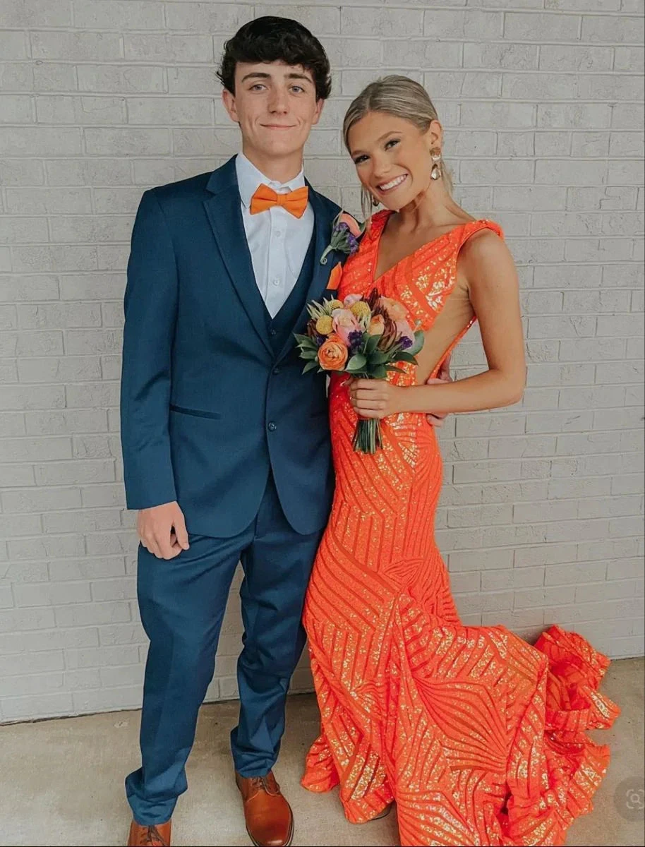 Young couple in formal attire, man in navy suit, woman in orange sequin gown with bouquet