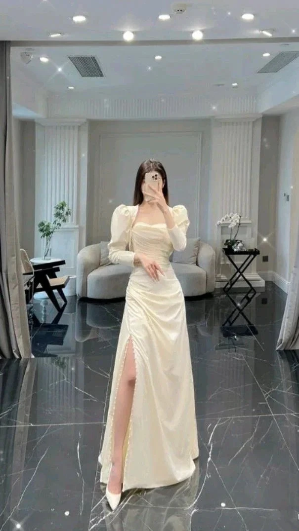 Woman in elegant cream puff sleeve gown with high slit, standing in modern living room, ZAPDRESS
