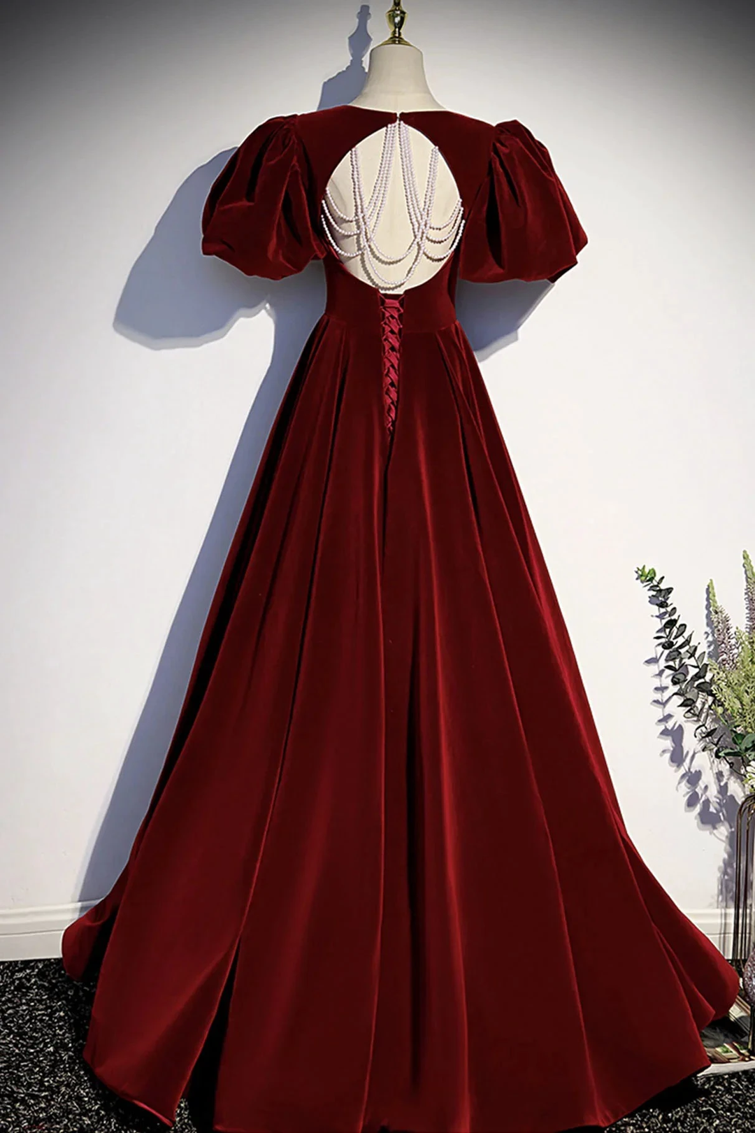 Elegant burgundy velvet evening gown with puff sleeves and pearl back details on mannequin