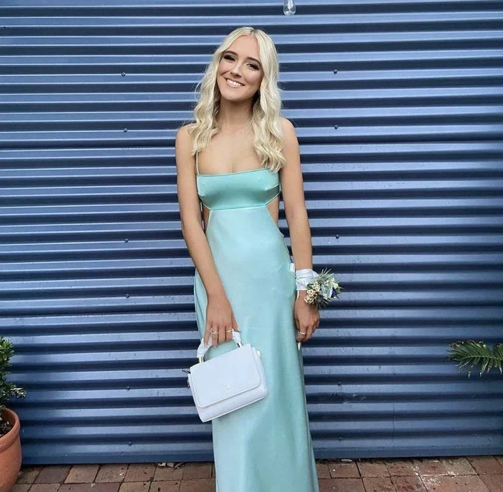 Woman in light blue satin prom dress holding white bag, standing in front of blue wall for ZAPDRESS