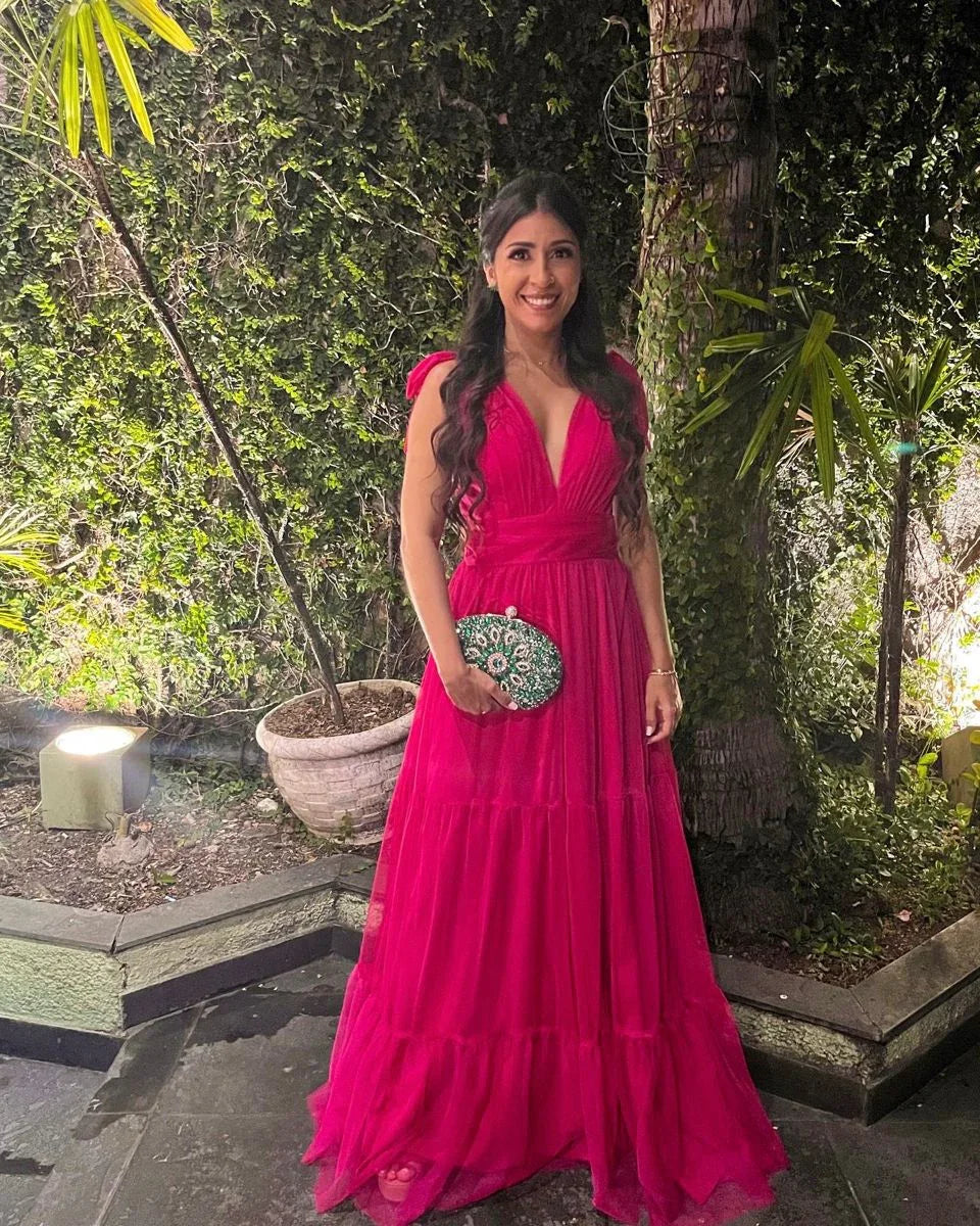 Woman in bright pink gown holding embellished clutch, standing in lush garden setting