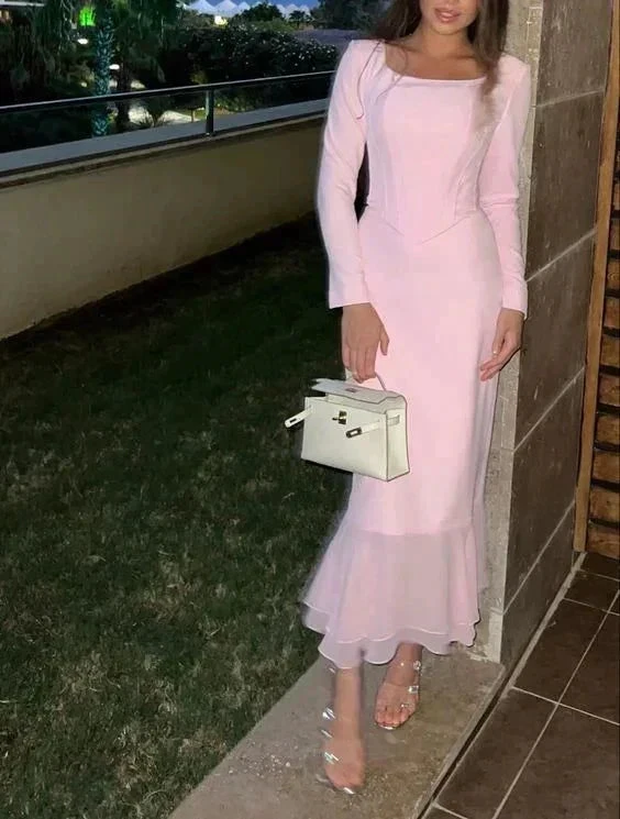 Woman in a long pink evening dress holding a white handbag, standing outdoors at night