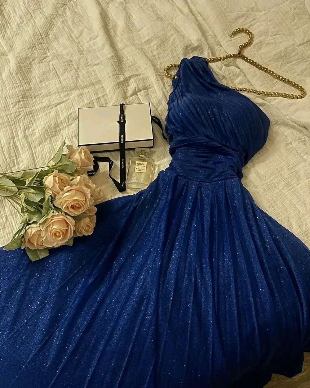 Elegant blue one-shoulder dress on bed with roses, Chanel perfume, and gift box, ZAPDRESS style