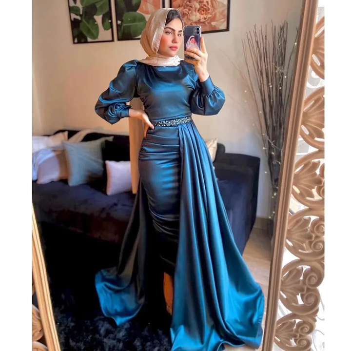 Woman in teal satin evening gown with hijab standing in modern living room, ZAPDRESS fashion