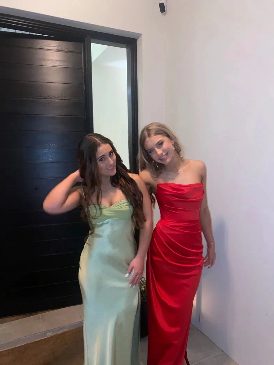 Two women in elegant satin evening gowns, one green and one red, posing indoors for ZAPDRESS
