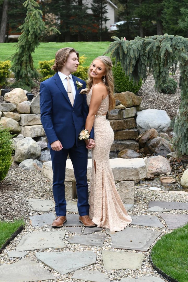 Young couple in formal attire, lace gown and navy suit, posing by garden rocks and greenery
