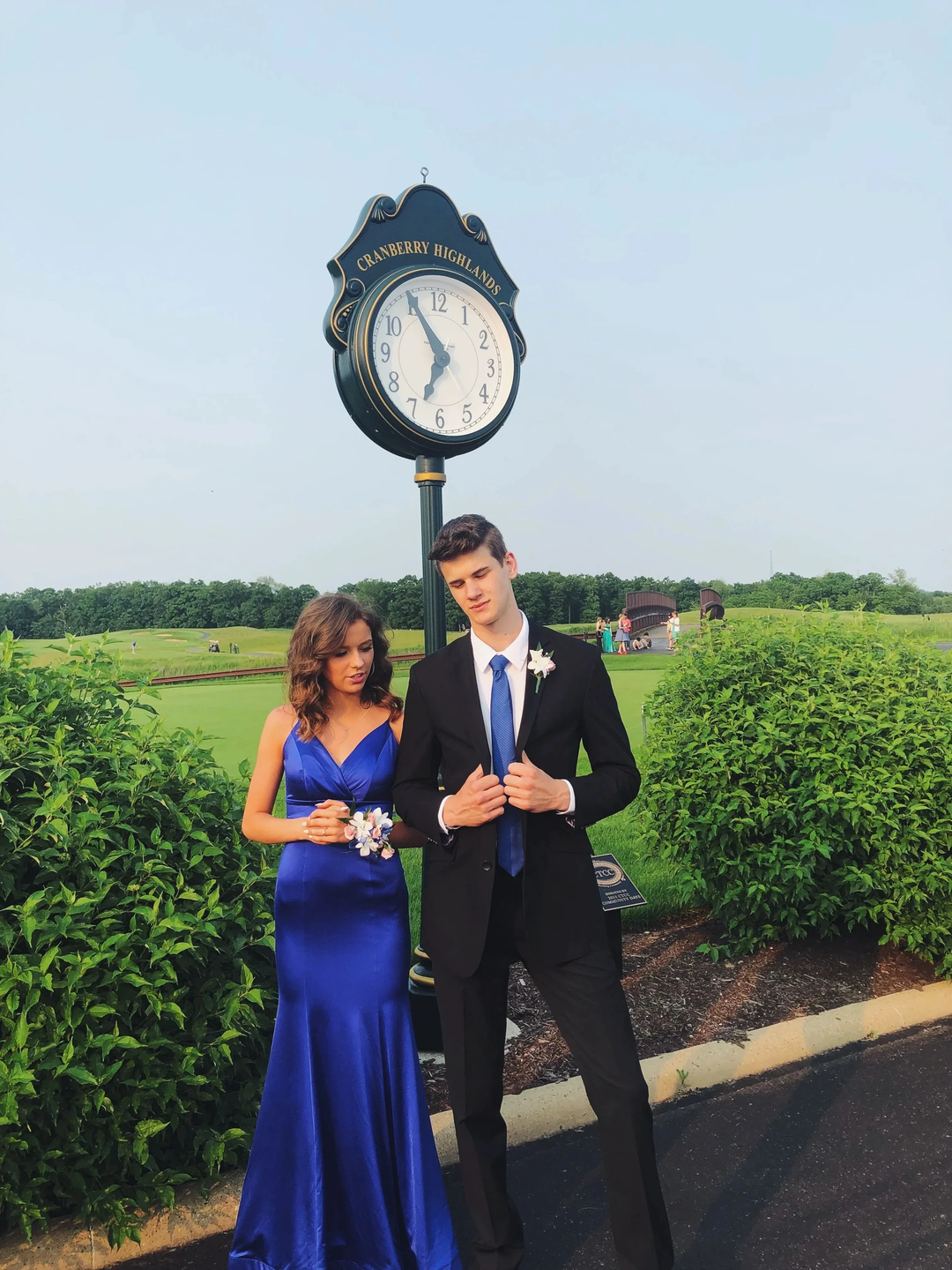 Couple dressed in formal blue attire at Cranberry Highlands golf course near outdoor clock, Zapdress style